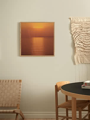 Stampa Still Copper in cornice di rovere su parete greige, accanto a un macramè crema appeso e a una sedia in pelle cuoio