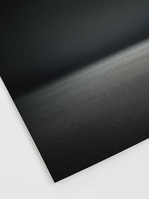 Primo piano in diagonale della stampa senza cornice che mostra la grana sottile dentro la morbida banda di luce nel buio