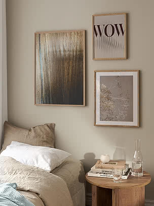 Druck Growth im Eichenrahmen als Teil einer Bilderwand aus drei Drucken über einem Bett mit beigen und weißen Kissen