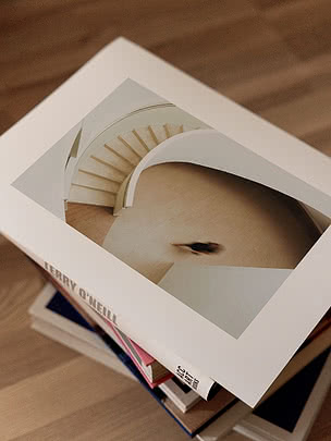 Helix print with a wide white margin lying on a stack of art books on a wooden floor, seen from above