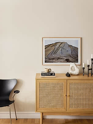 Druck Strata im Eichenrahmen an beiger Wand über einem Sideboard aus heller Eiche mit Rattanfronten, Büchern und schwarzen Leuchtern