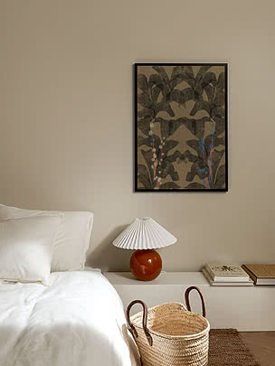 Trykket Botanical Symmetry i sort ramme på en beige soveværelsesvæg over en seng i hvidt hør og en plisseret lampe