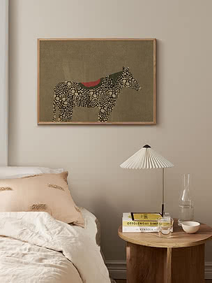 Druck Whimsical Horse im Eichenrahmen an beiger Wand über einem Bett mit rosé Kissen und einem runden Beistelltisch aus Holz