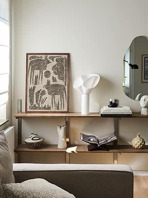 Desert Wildlife print in a wooden frame leaning on a shelf beside a white sculptural lamp and a mirror