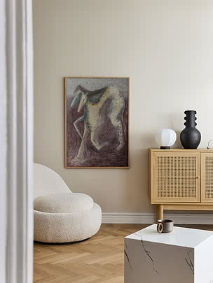 Poster The Hunt im Eichenrahmen an cremeweißer Wand über einem runden weißen Bouclé-Sessel, neben einem Eichensideboard mit schwarzer Rillenvase