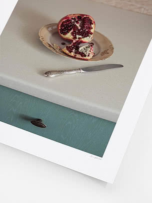 Close-up of the print showing pomegranate seeds, the silver knife and the sage green cabinet below the counter
