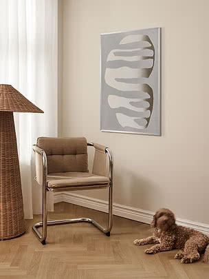 Gradient poster in a pale frame on a beige wall beside a rattan floor lamp and a chrome and leather chair