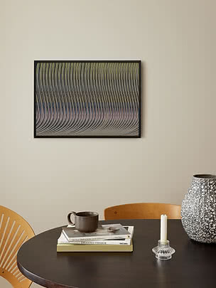 Poster Iridescent im schwarzen Rahmen an beiger Wand über einem runden dunklen Tisch mit Büchern, brauner Keramiktasse, einer Kerze und gesprenkelter grauer Vase