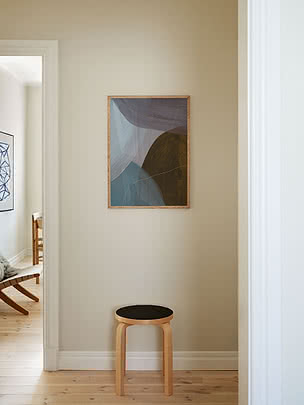 Trycket Harmony in Umber i ekram på en beige hallvägg ovanför en trebent pall med svart sits