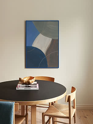 Trycket Harmony in Blue i blå ram på cremefärgad vägg ovanför ett svart runt matbord med stolar i papperssnöre