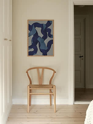 Trykket Ultramarine Swirls i egeramme på en cremefarvet entrévæg over en Wishbone-stol i lys eg