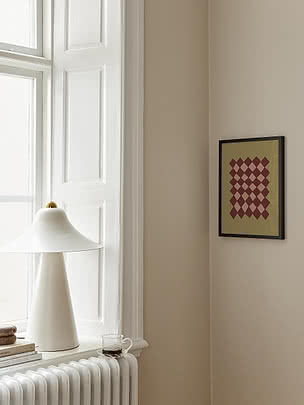 Affiche Earthy Diamond Pattern dans un cadre noir fin sur un mur beige dans un coin fenêtre, près d'une lampe conique blanche sur l'appui et de livres sur un radiateur