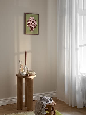 Retro Checkered Vase poster in a dark red frame on a beige wall above a round oak side table with a terracotta candle, brushes in a pale vessel and small bowls