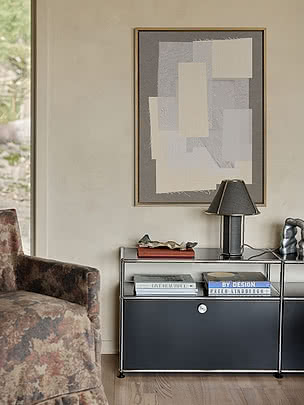 Affiche Textile Harmony dans un cadre en chêne sur un mur en enduit au-dessus d'un buffet chromé gris foncé avec une lampe, des livres et une sculpture en métal