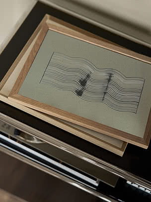 Poster Wavy Reflections I im Rahmen aus heller Eiche, auf einem Stapel Rahmen auf einer dunklen polierten Fläche liegend, schräg von oben gesehen