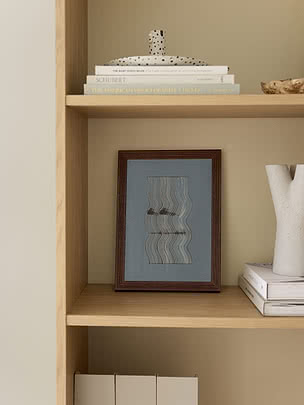 Poster Wavy Reflections II im dunklen Holzrahmen, auf einem Eichenregal stehend, neben einer weißen skulpturalen Vase und Büchern, mit einer gepunkteten Keramikfigur im Regal darüber
