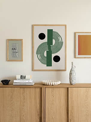 Plakat Modern Objects Green w dębowej ramie na kremowej ścianie nad dębową komodą, powieszony między małym oprawionym plakatem a plakatem z ciepłym gradientem, z książkami i cętkowanym wazonem butelkowym