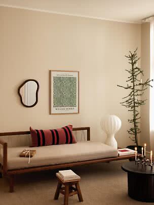 Hyggelig stue med trædaybed, rødstribet pude, papirlampe, slankt grantræ og tændte lys