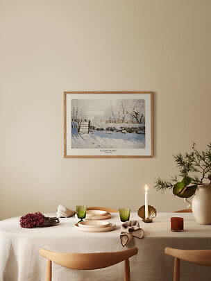 Framed Claude Monet winter print above a set dining table with candle, green glasses and branch vase