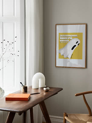 Poster giallo incorniciato con fantasma illustrato sopra un tavolo in legno vicino alla finestra