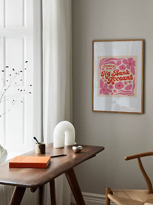 Gerahmter rosa-oranger Typografie-Print mit Blumen an beigefarbener Wand über Holztisch