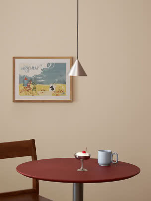 Small silver pendant lamp above a red table with mug and dessert in a bright room