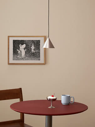 Lampada a sospensione conica argento sopra tavolo rosso con tazza blu, dessert e stampa incorniciata