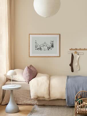 Hyggeligt børneværelse med beige seng, puder, lille hvid lampe og vægkunst i træramme