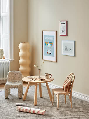 Angolo bimbi accogliente con tavolino in legno, due sedie, lampada da terra e poster dei Moomin