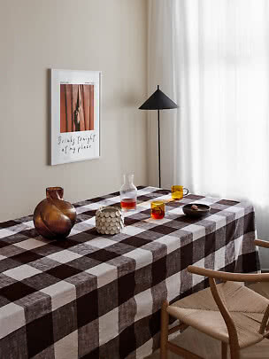 Table à manger avec nappe à carreaux bruns, verres, vase et lampadaire noir près de la fenêtre