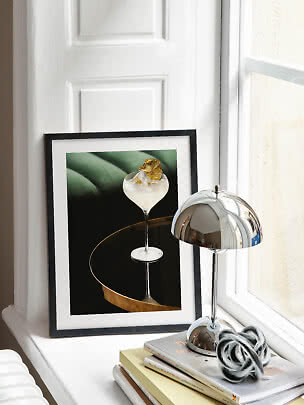 Framed poster of a cocktail glass with ice and dried citrus on a windowsill beside a chrome lamp