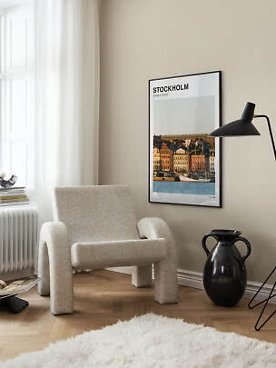 Stockholm-Poster im schwarzen Rahmen über hellem Sessel in einer stilvollen Zimmerecke.