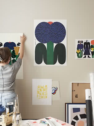 Persona appende un poster artistico colorato con fiore blu su parete beige in studio