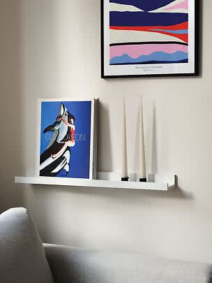 Weiße Wandablage mit Kunstbuch, zwei Kerzen und buntem Poster über einem grauen Sofa