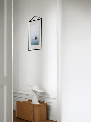 Weiße Tischlampe mit rundem Schirm auf Holzschrank vor weißer Wand mit gerahmtem Bild