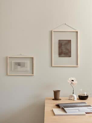 Two light wood frames on a beige wall above a wooden table with a vase, carafe and open book.
