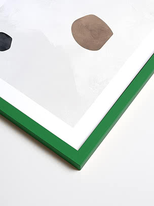 Primo piano in diagonale dell’angolo di una cornice quadrata in verde, con passepartout bianco e una stampa astratta sotto vetro