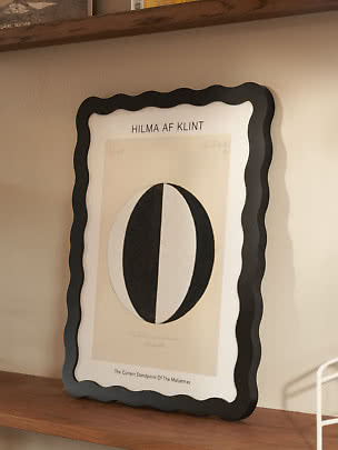 Affiche Hilma af Klint encadrée avec cadre noir ondulé sur une étagère en bois