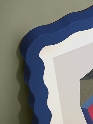 Nahaufnahme eines Spiegels mit welligem blauem Rahmen an olivgrüner Wand