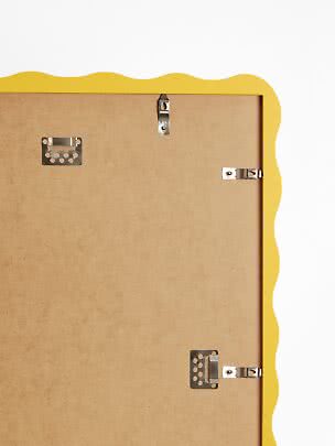 Back of yellow picture frame with wavy edge and metal hanging hardware