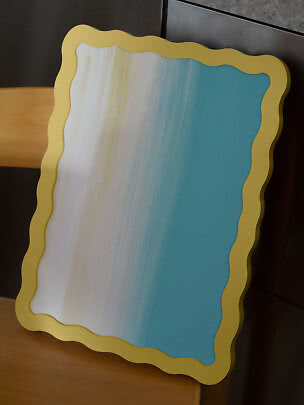 Rectangular mirror with wavy gold frame and blue-tinted glass, leaning against a wooden chair