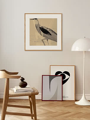 Poster con airone in passepartout bianco e cornice in rovere su una parete beige, sopra uno sgabello di legno e una piantana