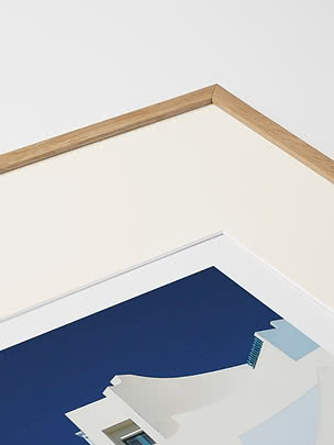 Primo piano in diagonale dello smusso di un passepartout in crema dentro una cornice in rovere, con un poster blu sotto vetro