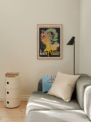 Affiche encadrée Loïe Fuller au-dessus d’un canapé gris, coussins, lampe noire et table blanche