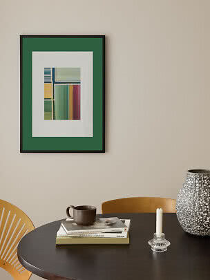 Framed abstract art print with green mat above a round table with vase, candle holder and books
