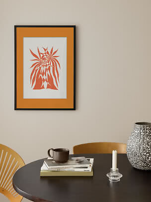 Framed orange abstract art print on a beige wall above a black table