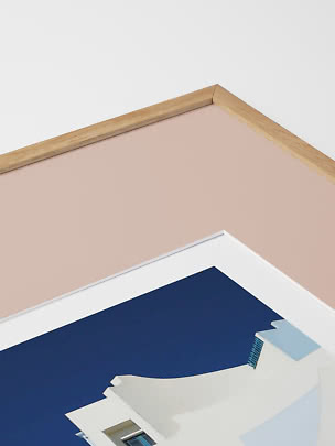 Close-up of framed art print with light wood frame and white building against blue sky