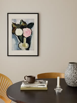 Framed floral print in a black frame above a table with books, mug, candleholder and large vase