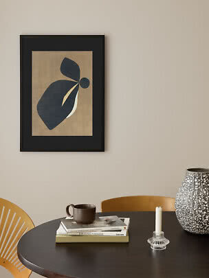 Black framed abstract print with dark organic shapes on a beige wall above a dining table