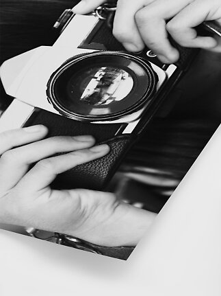 Primo piano in bianco e nero di mani che tengono una fotocamera vintage con grande obiettivo